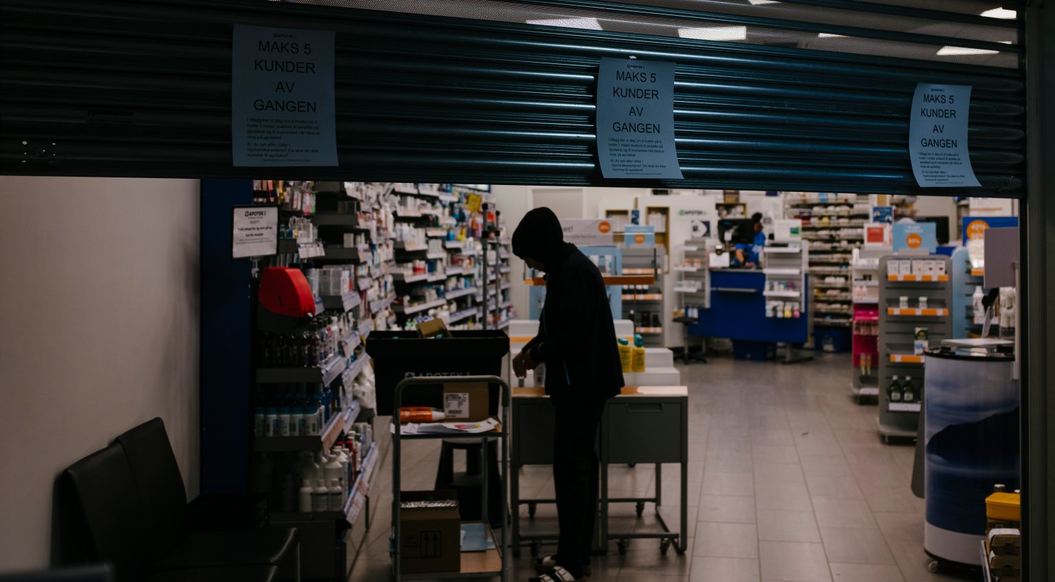 Apotek som er i ferd med å stenge. Mørkkledd person foran hyller med medisiner.