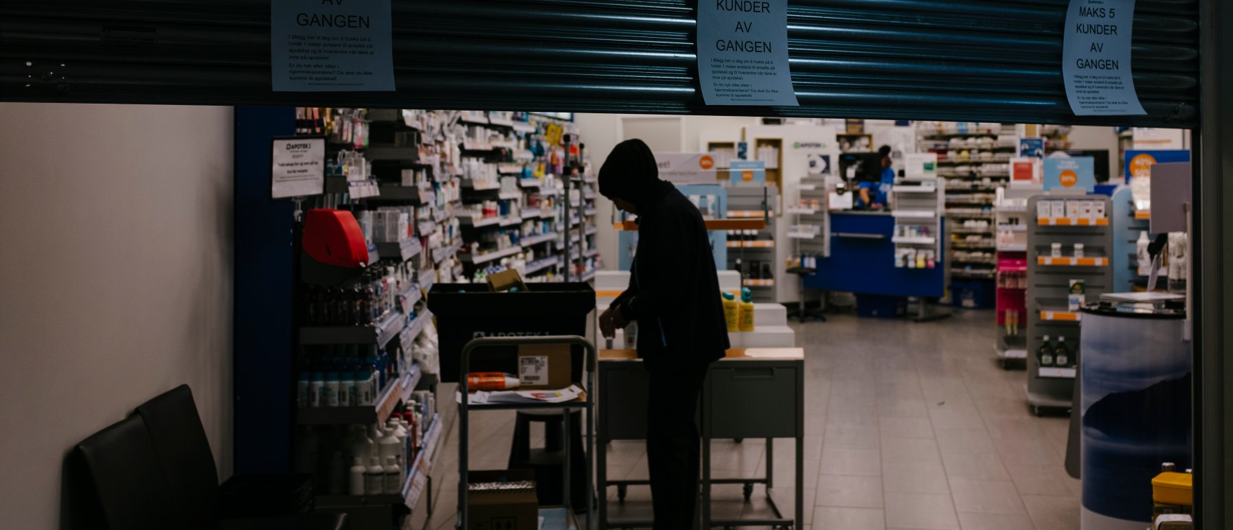 Apotek som er i ferd med å stenge. Mørkkledd person foran hyller med medisiner.