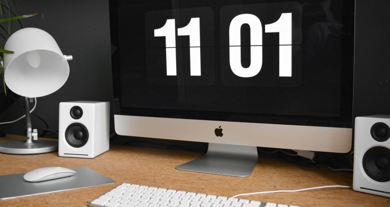 Mac-skjerm på et skrivebord, med en stor digital klokke.