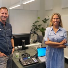 Eirik Bergesen (t.v) og Mari Mellum i podkast-studioet. I bakgrunnen ser du teknisk utstyr, begge to smiler til kamera.