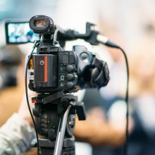 Television camera recording publicity event. Camera in focus, operator and event blurred